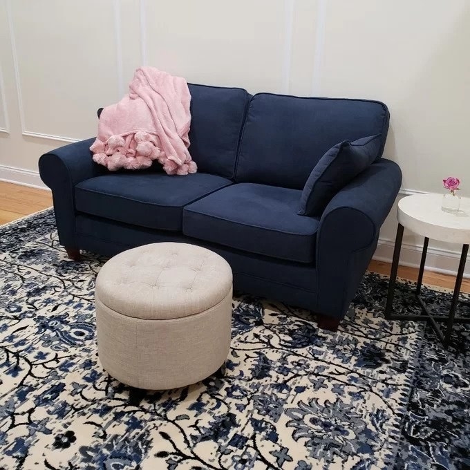 Beige upholstered round ottoman in front of navy couch
