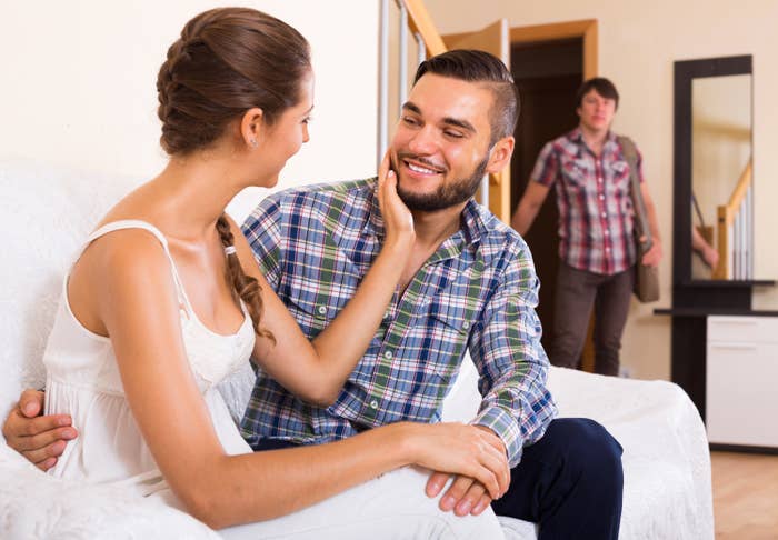A woman flirts with a man at home as her husband enters the room