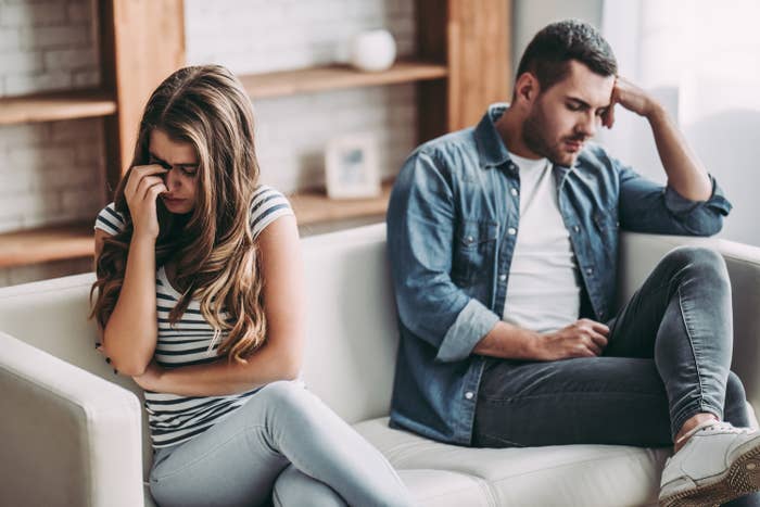A couple faces away from one another as they argue on the couch at home