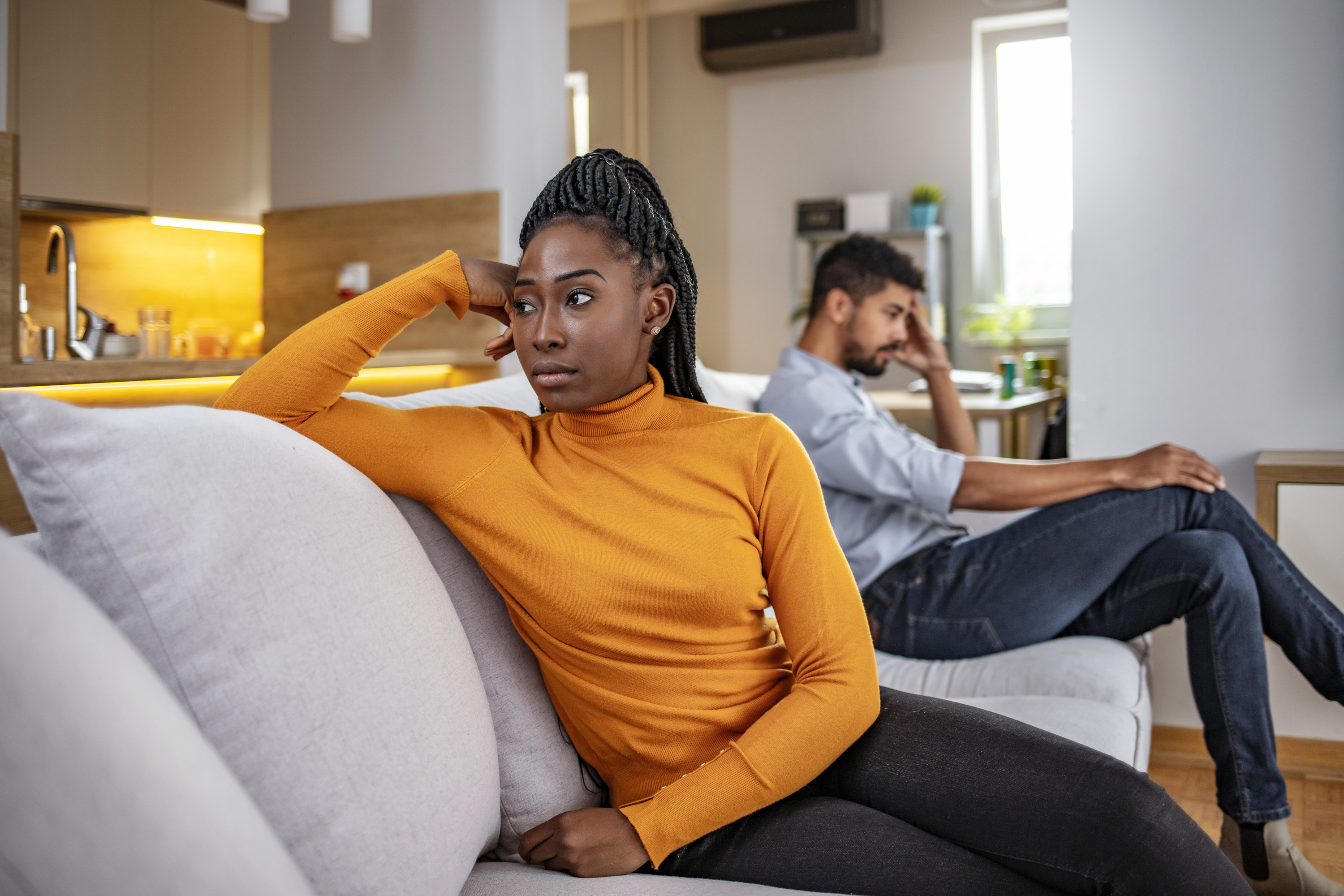 A woman faces away from her partner with a sad look on her face while sitting on the couch