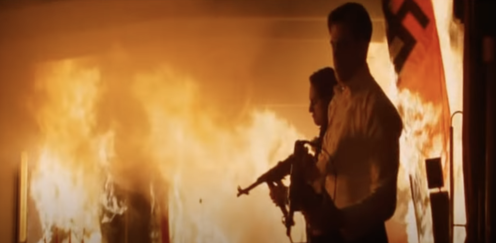 Two men prepare guns as a theater goes up in flames around them