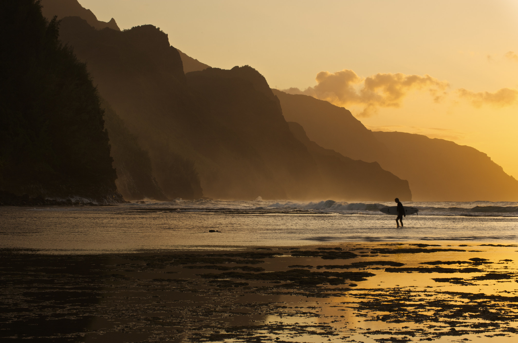 Surfer on beach and Na Pali Coast seen from Ke'e beach.
