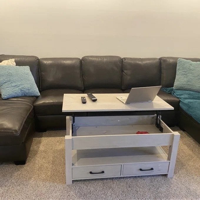 White lift top coffee table with top lifted to reveal storage underneath, laptop and remotes on table top