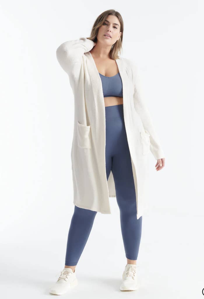 a model wearing the cardigan over a pair of leggings and a sports bra