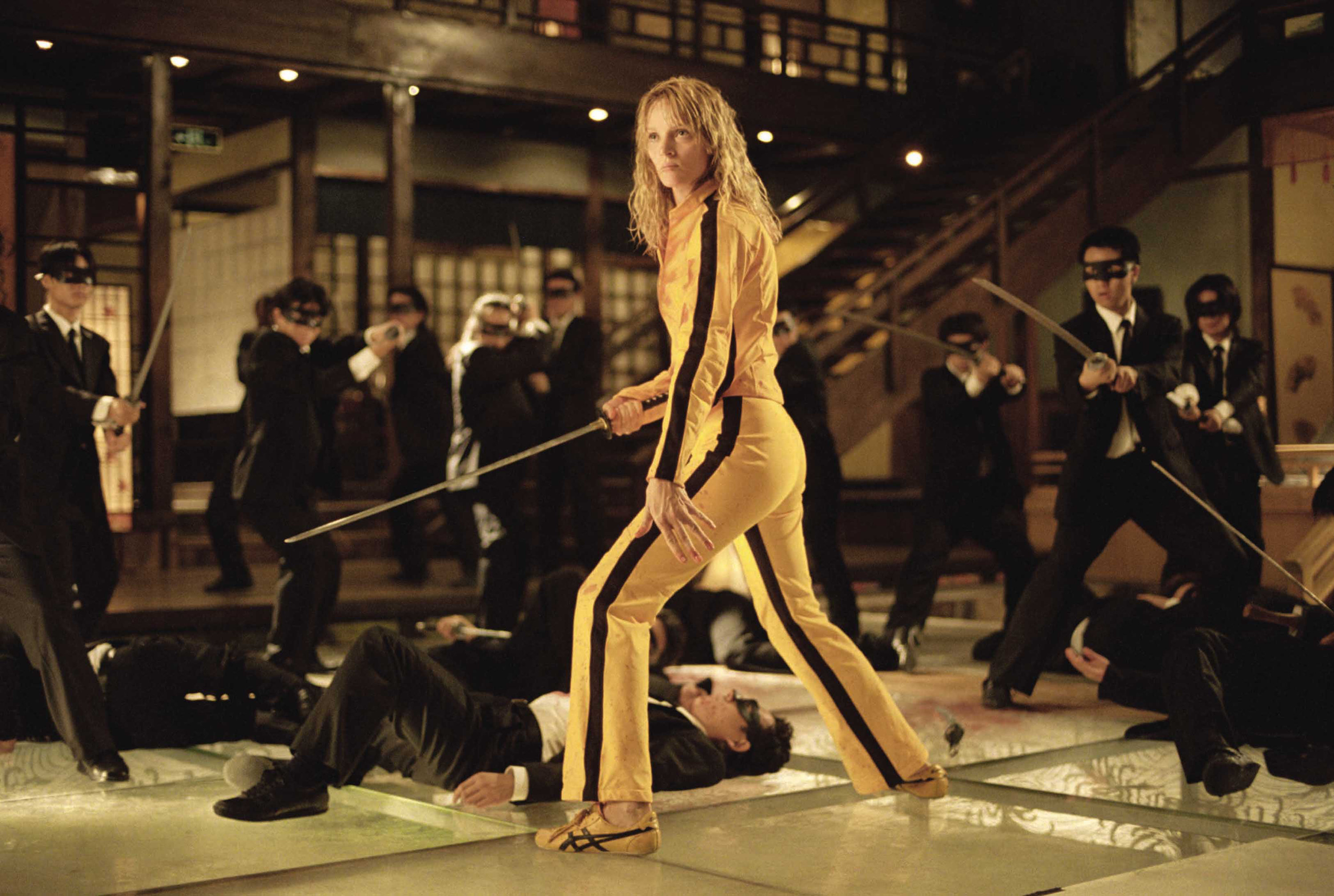 Uma Thurman in a yellow and black jumpsuit holds a samurai sword near a number of assailants