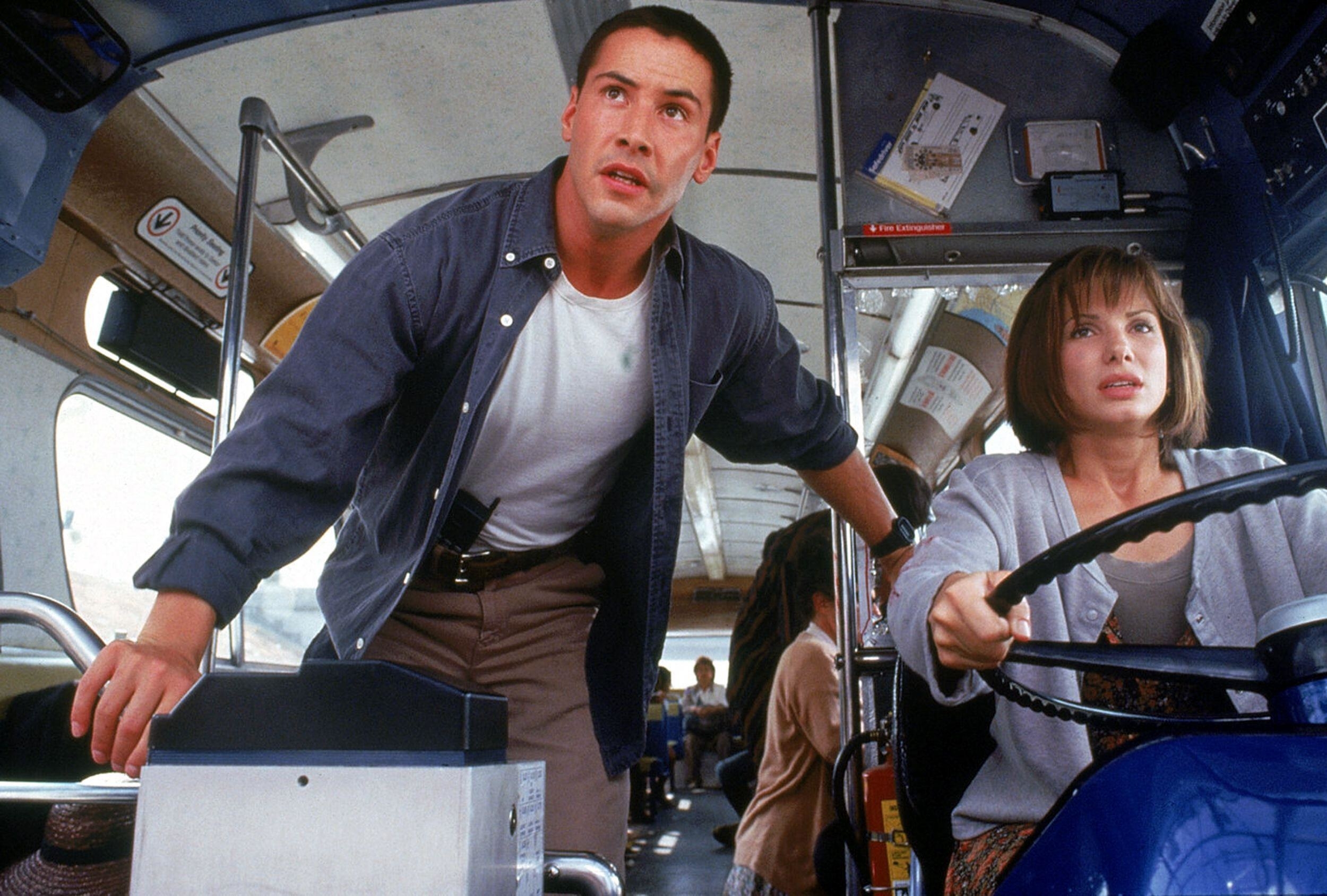 Keanu Reeves and Sandra Bullock stare with concern as Sandra drives a bus