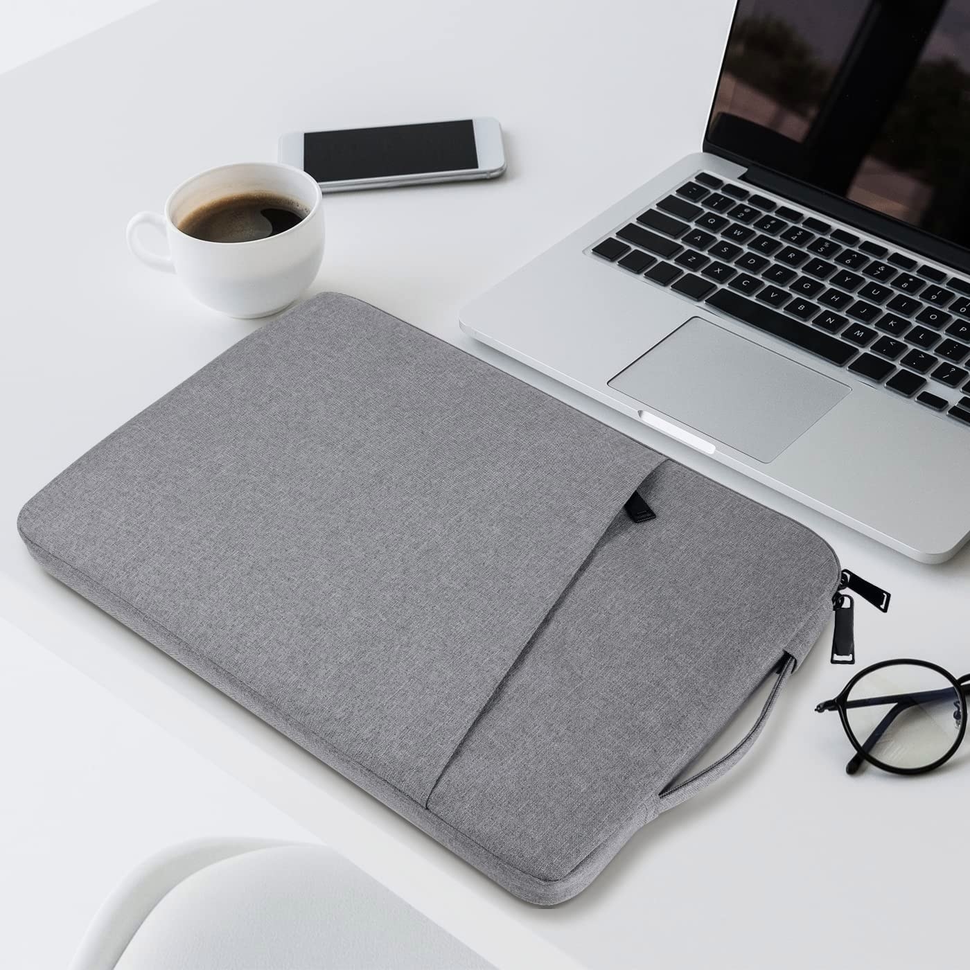 a laptop sleeve on a clean surface next to a laptop, phone, and coffee