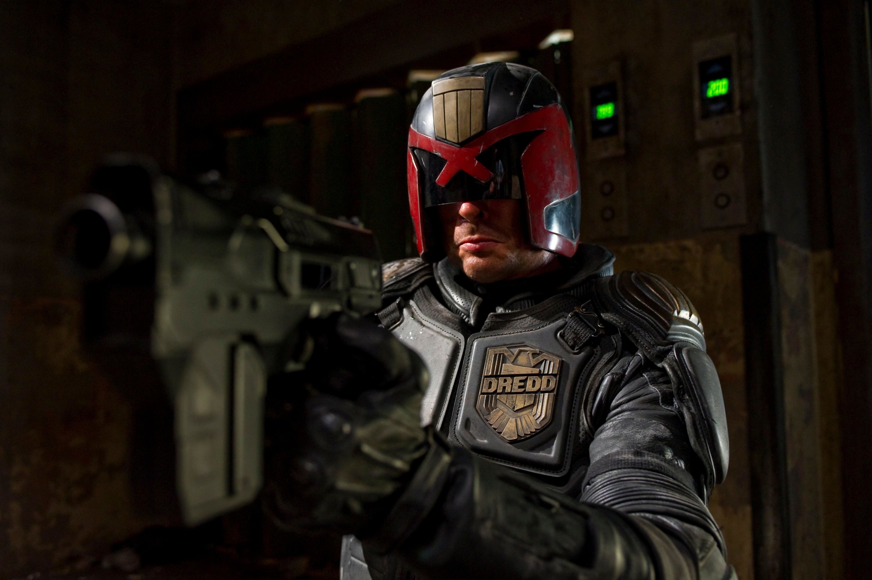 Judge Dredd holds a large futuristic handgun to the camera