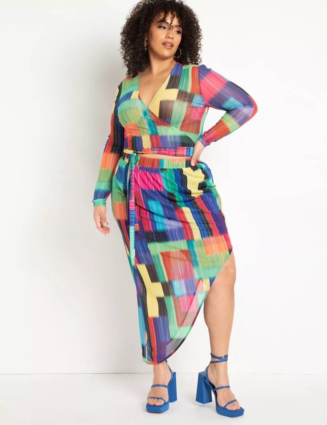 Model wearing matching long sleeve wrap shirt and asymmetrical midi skirt set, multicolored pattern, paired with blue sandal heels