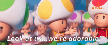 A toad from Super Mario Bros. with arms open and gesturing to the other toads while saying &quot;look at us we're adorable&quot;