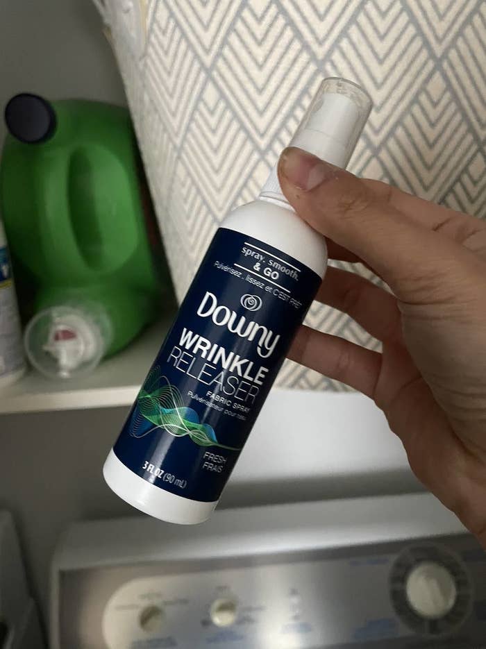 may holding a bottle of downy wrinkle releaser spray in her laundry room