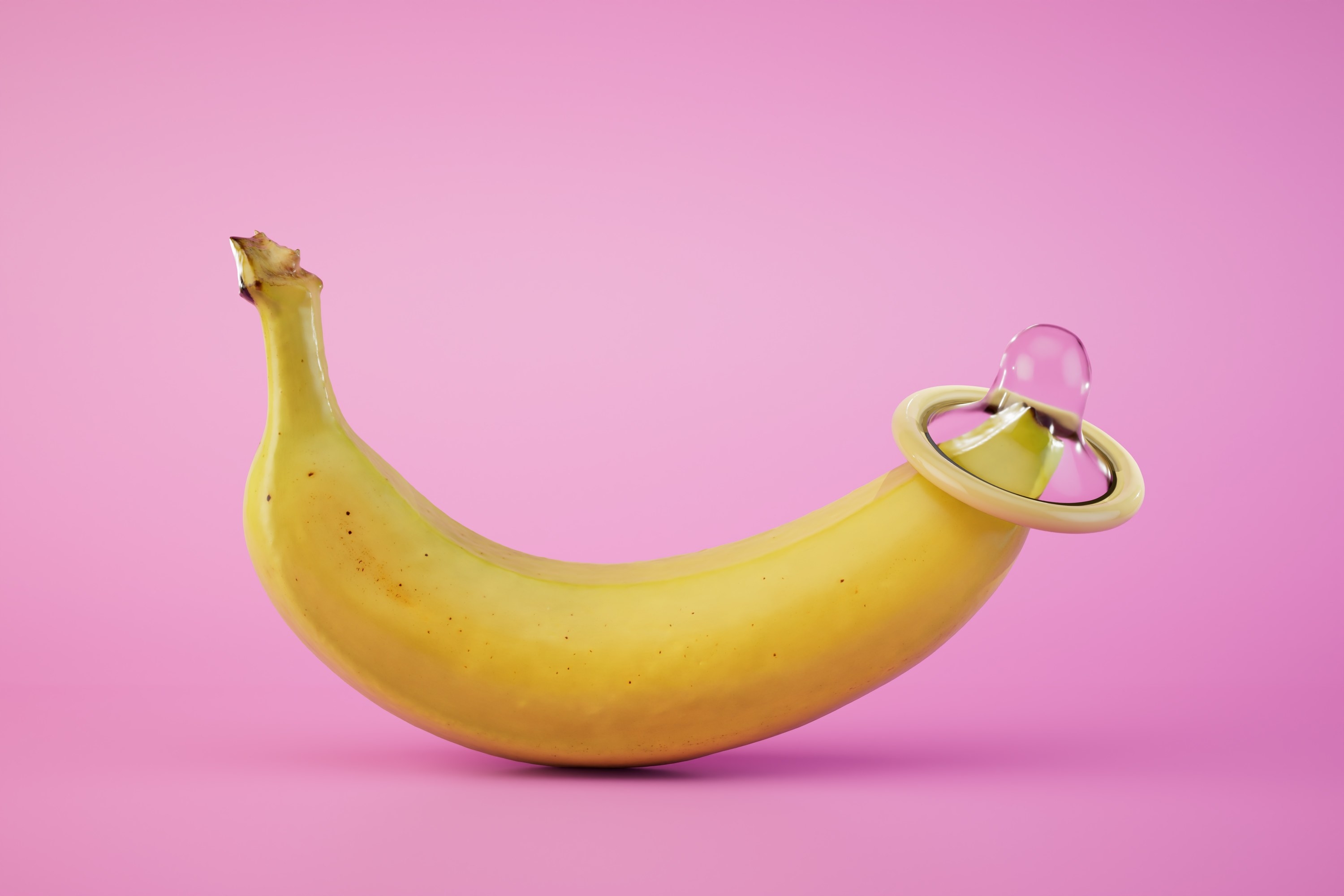 a condom worn on the tip of a banana in front of a pink pastel background