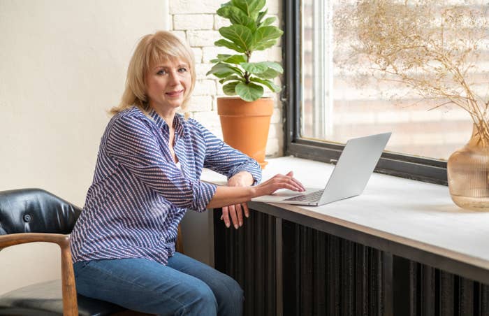 A woman sitting by a window while working on a laptop