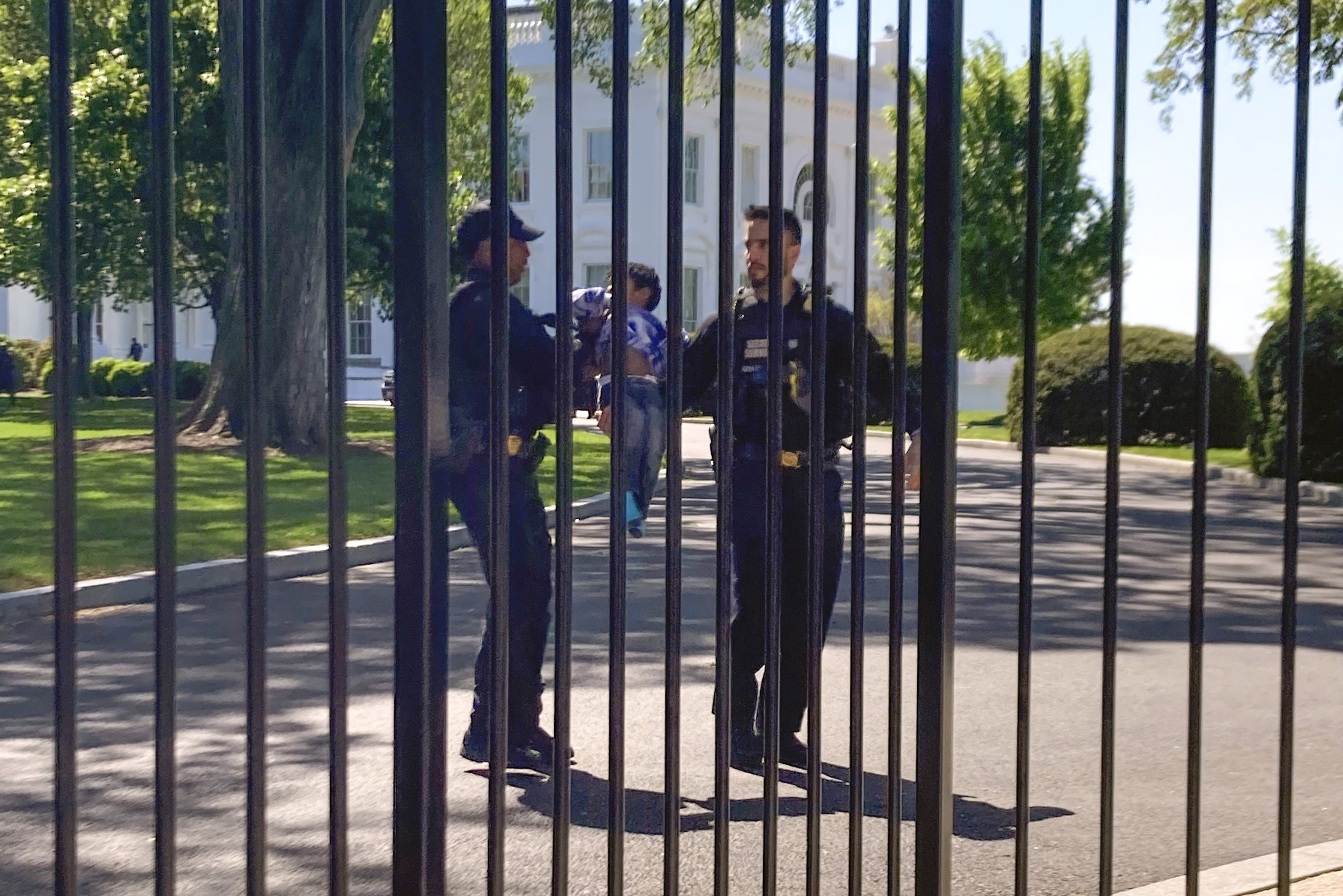 Two security guards hold up the toddler behind the gates