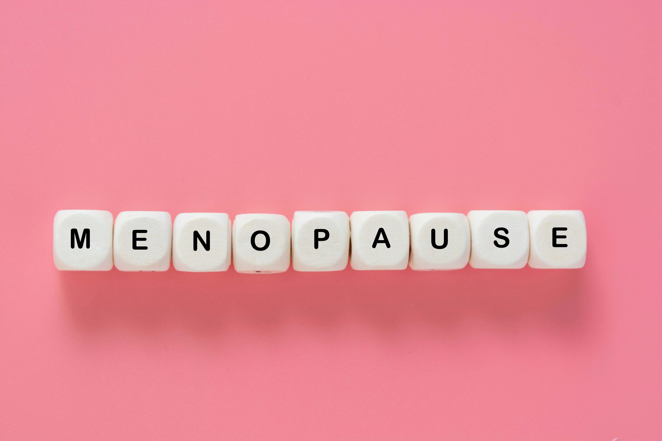 Menopause word abstract text, wooden blocks over pink background, top view