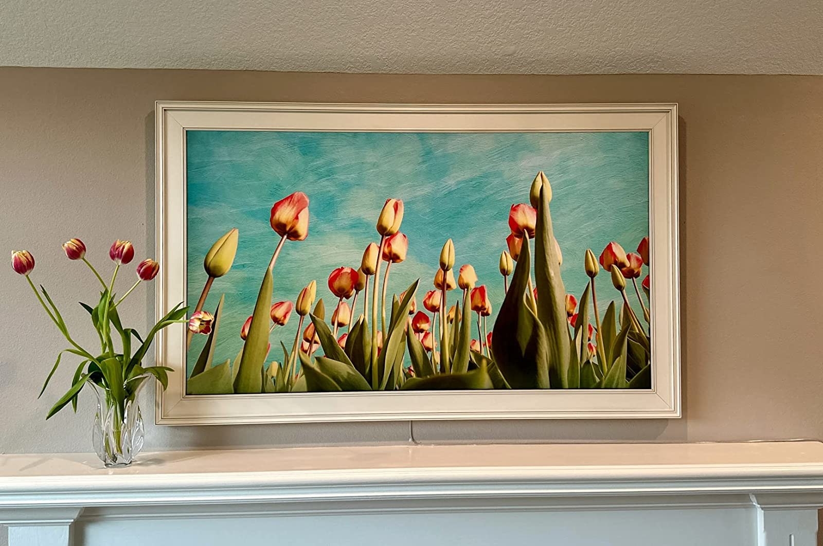 a review photo of the television hung over a mantle with a picture of flowers that looks like a painting