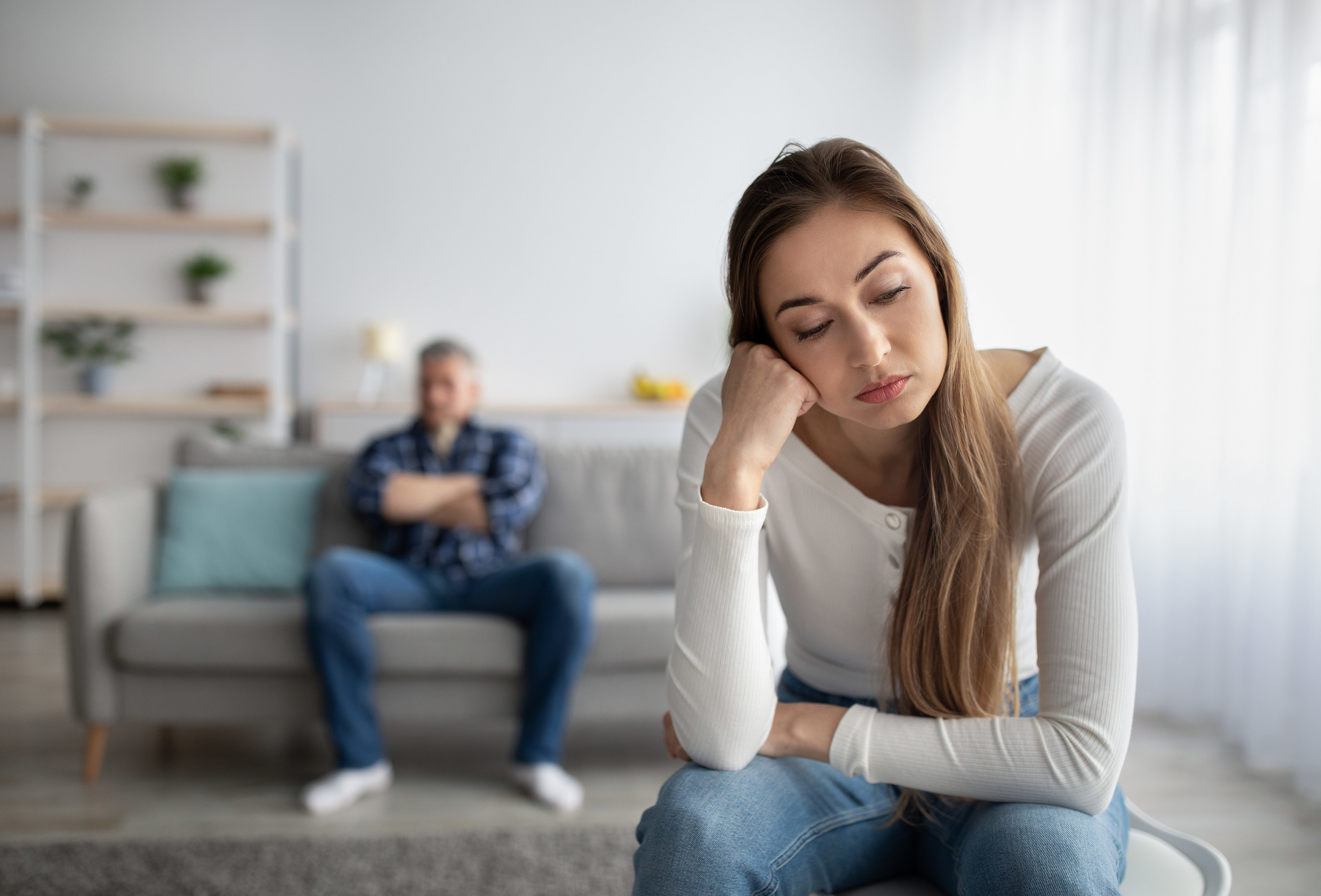 A woman looks upset as she sits at a distance from her partner at home