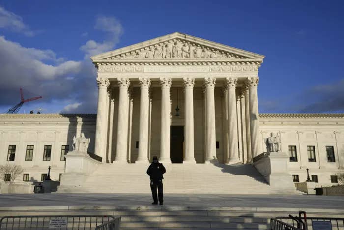 a security guard stands outside the supreme court on a sunny day