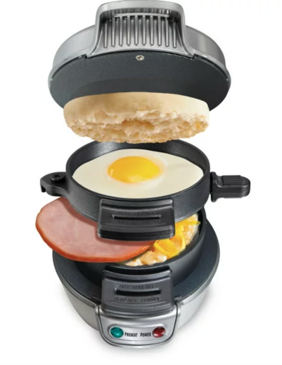 the silver and black sandwich maker, filled with an english muffin, egg, ham and cheese