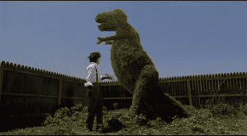 Edward Scissorhands trimming a large hedge into a dinosaur