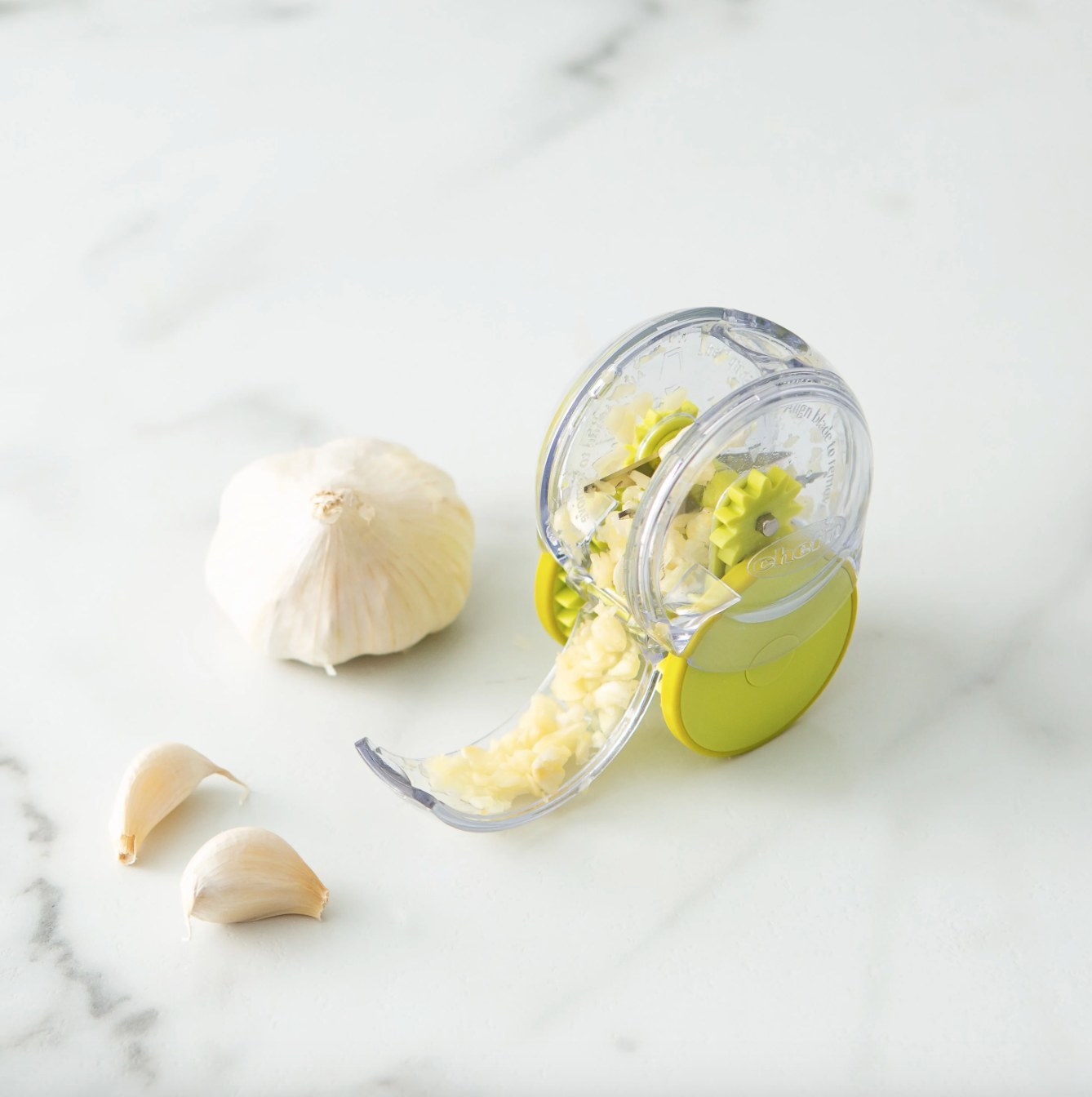 the clear and green chopper next to a head of garlic and two cloves