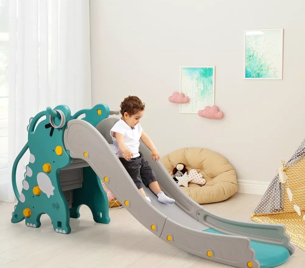 child sliding down the slide on the gray and green dinosaur-themed climber slide play set