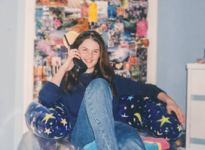 A young girl sitting in a colorful print chair and holding a huge phone with an antenna to her ear