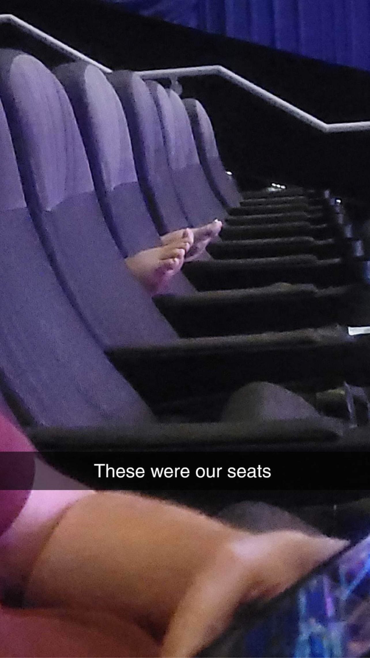 Two feet resting on the arms of a theater seat