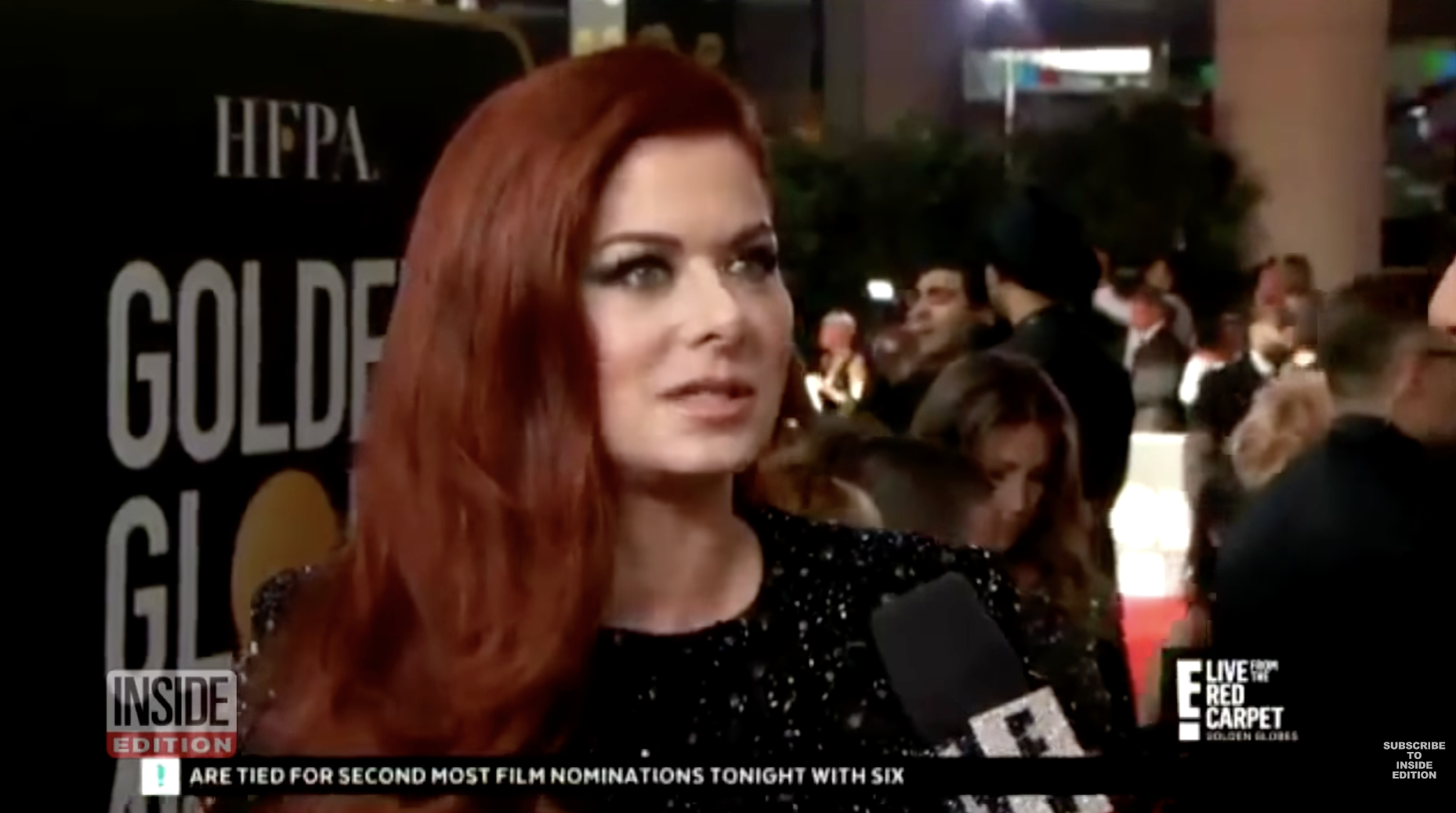 Debra Messing in a sparkly black dress with the Golden Globes red carpet behind her, being interviewed by E!