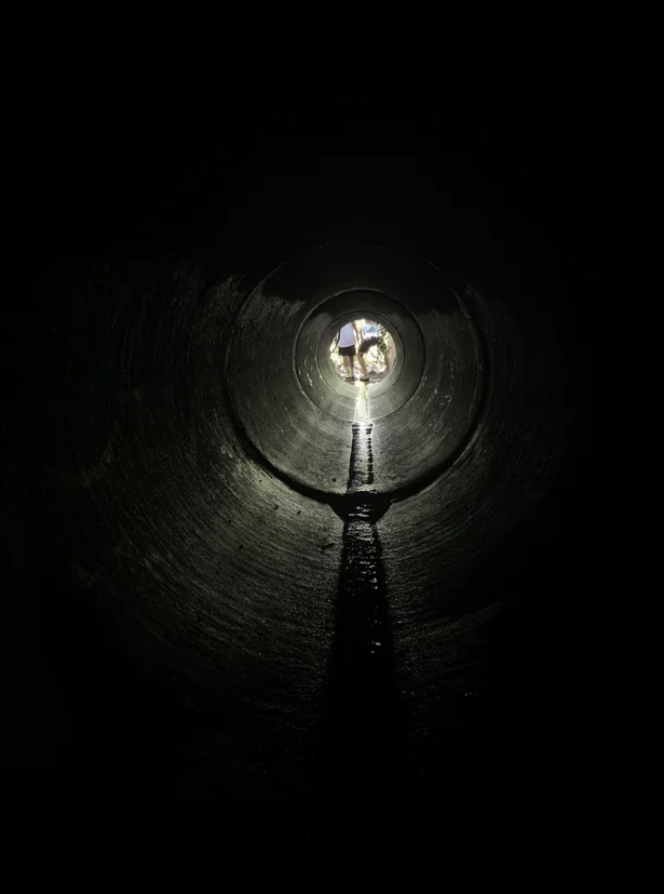 An empty storm drain with two people visible at the top