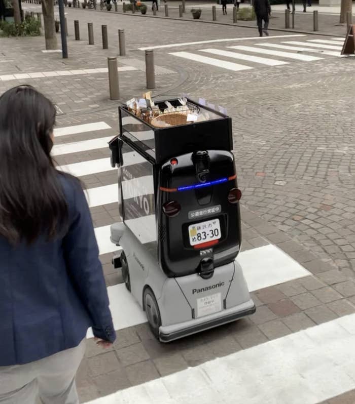 An unmanned robot on wheels rolls across a crosswalk while carrying snacks and sauces