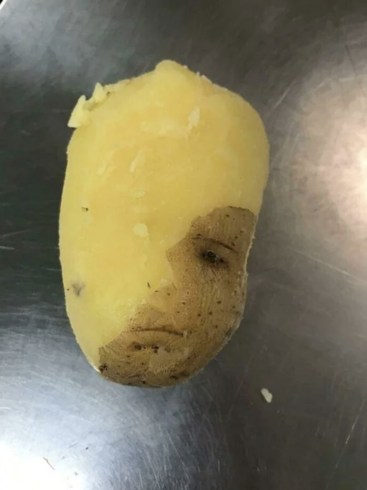 Close-up of a half-peeled raw potato, with one &quot;eye&quot; visible and what looks like a mouth
