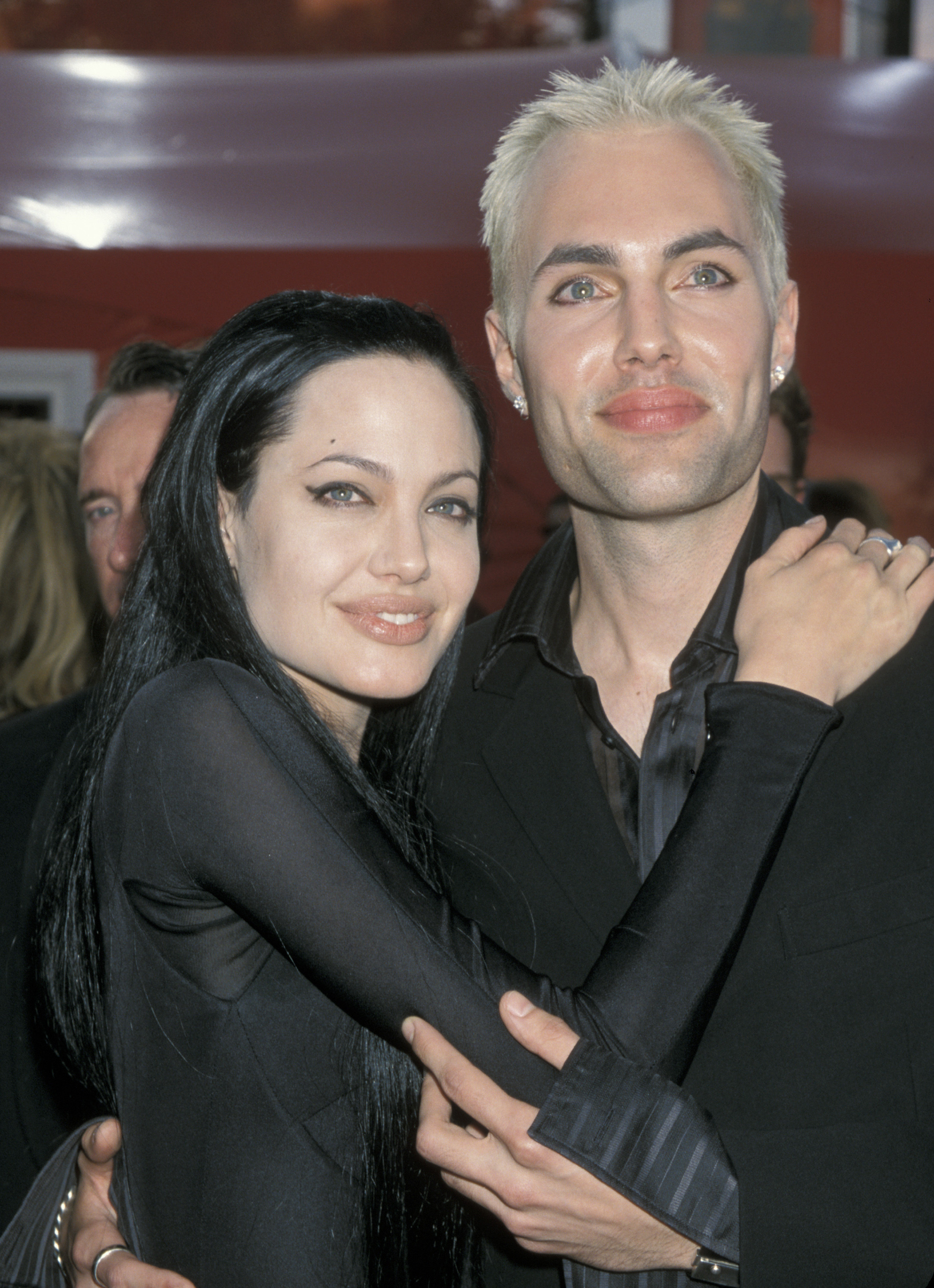 Angelina Jolie and James Haven wear all black and stand posing for a photo with their arms around each other