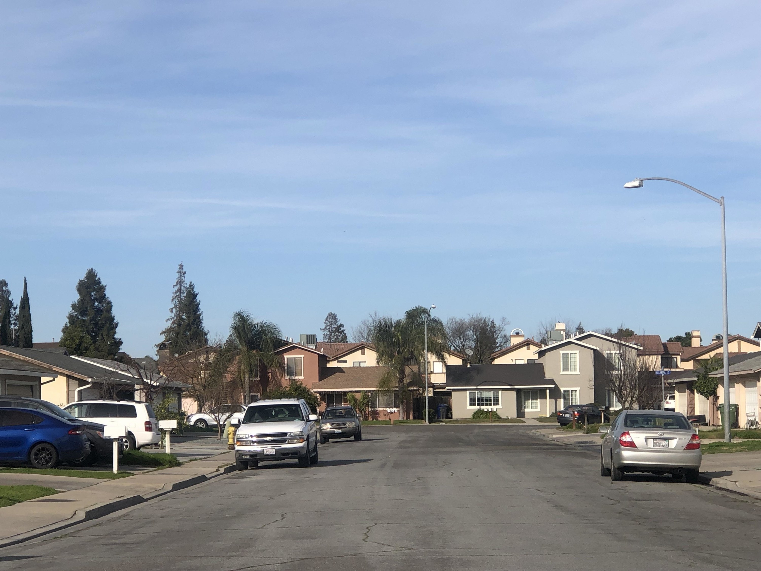 A dead-end in a suburban neighborhood featuring average-sized houses with driveways and cars parked in the street