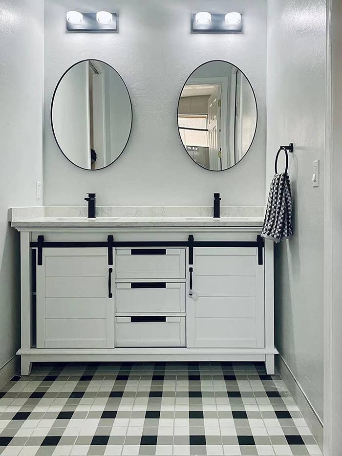 A reviewer&#x27;s photo of two oval mirrors hung in the bathroom