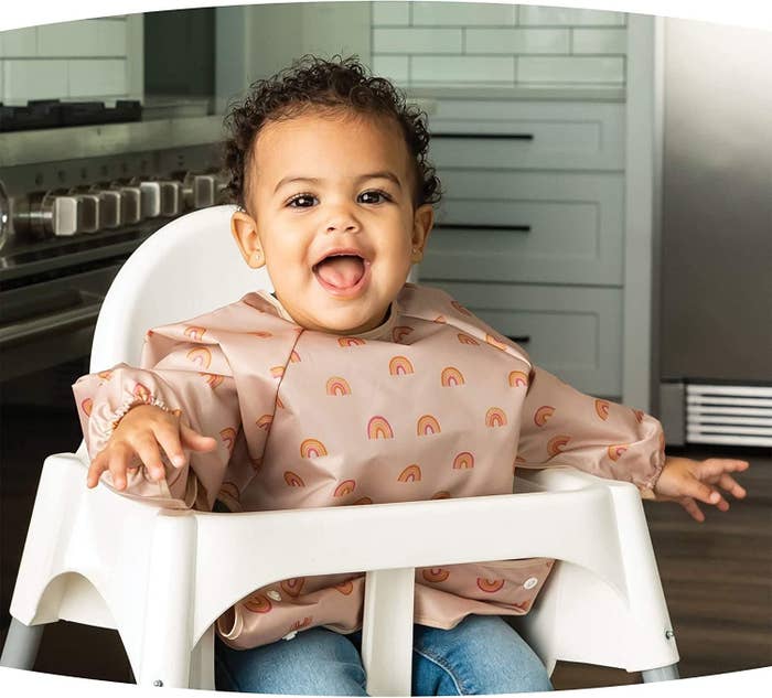 baby sitting in high chair and wearing pink bib with rainbow pattern