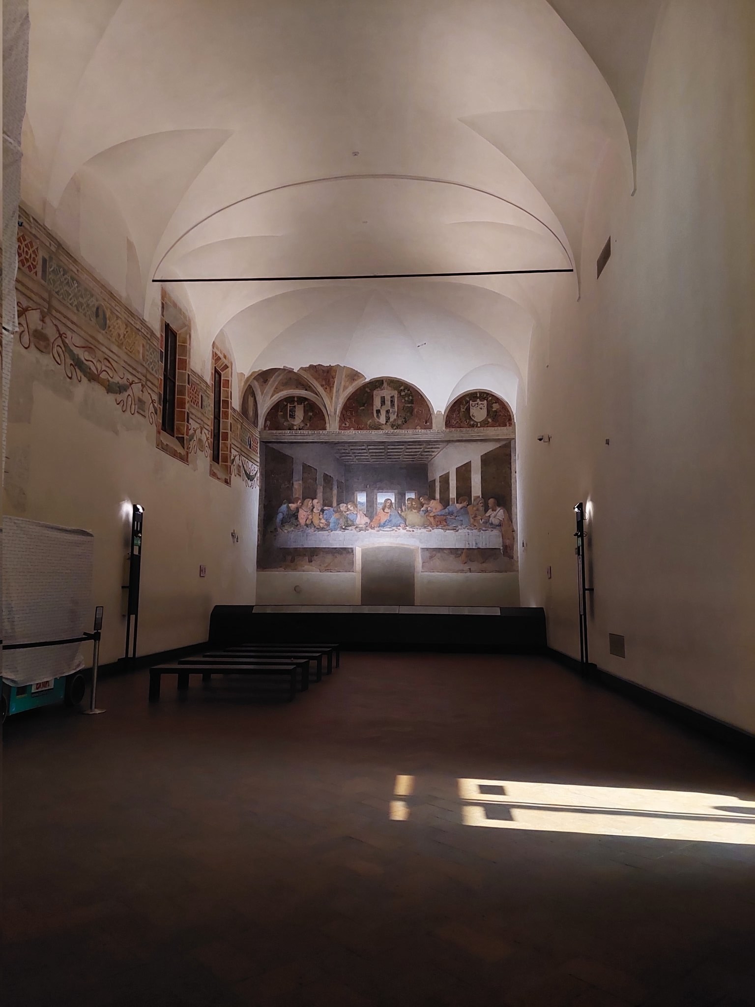 A medium-size painting inside the refectory of a small convent, with two small lights illuminating it