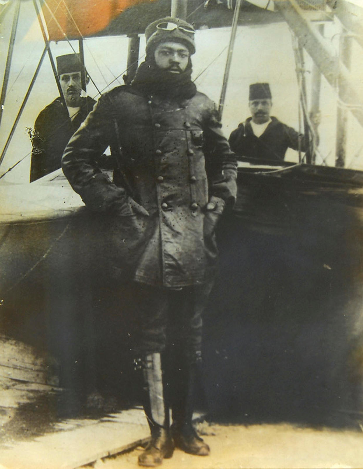 A man with high boots and in a uniform stands in front of an early plane