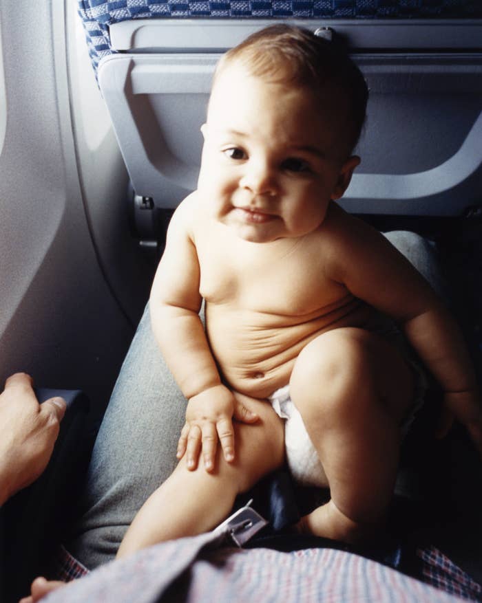 A baby sits on an adult's lap during a plane ride