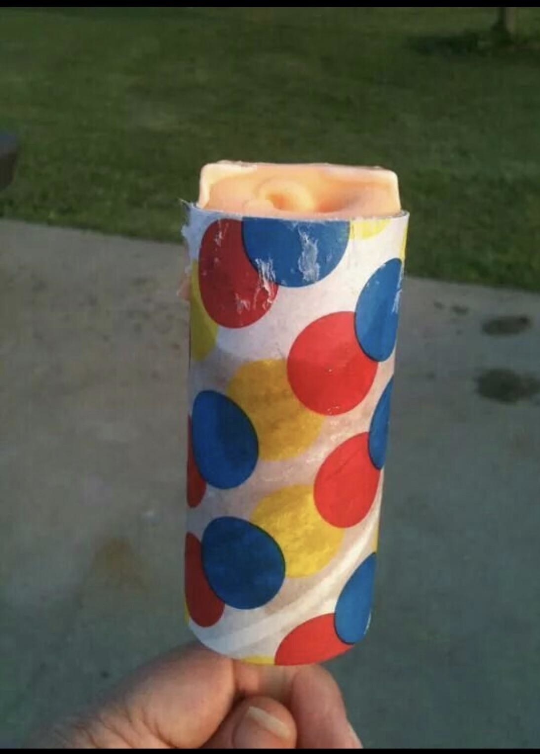 A hand grips a push popsicle that has a wrapper with primary colors on it