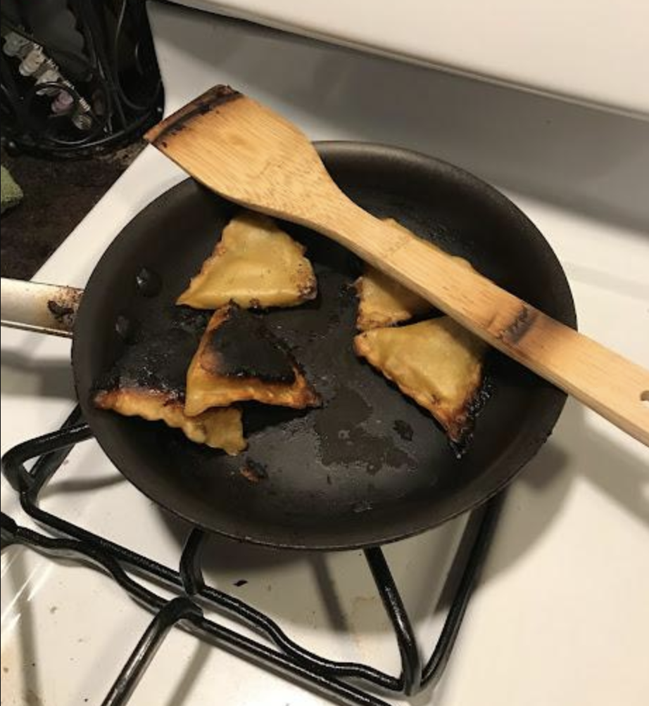 Burnt food in a pan on a stove with a burnt spatula