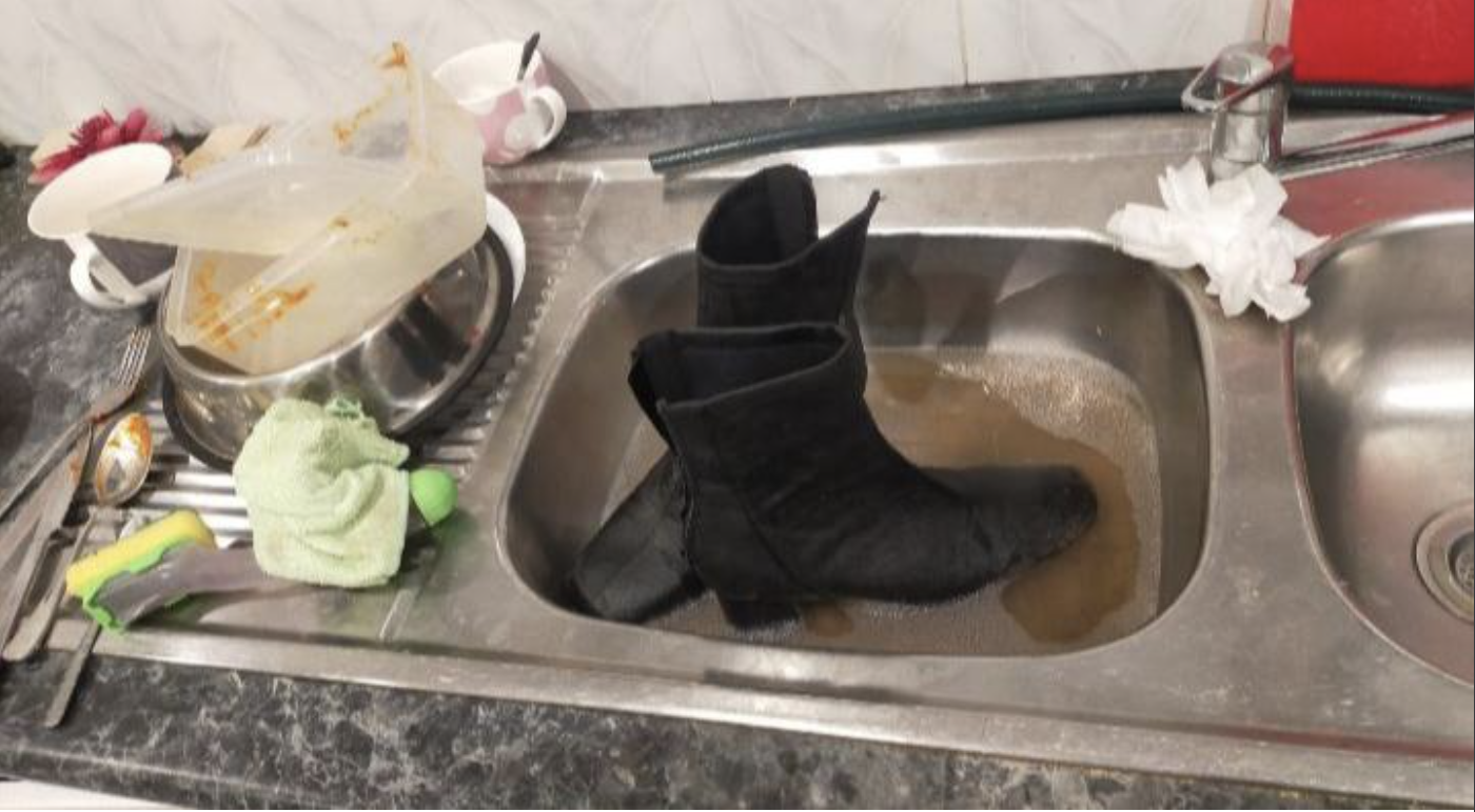 Black boots floating in a kitchen sink full of dirty water