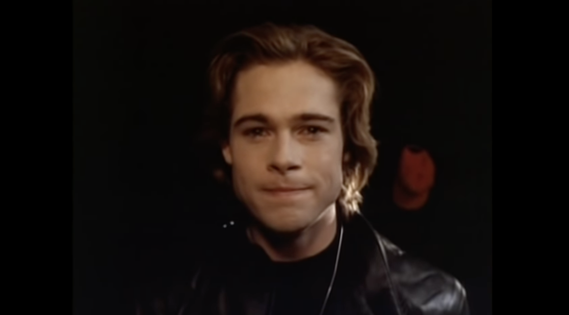 A young Brad Pitt wears all black and is looking directly into the camera with a small smile
