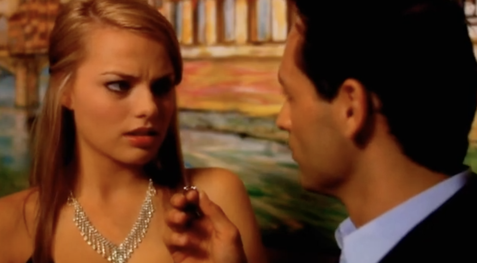 A young Margot Robbie is sitting at a restaurant looking at a man next to her with disgust