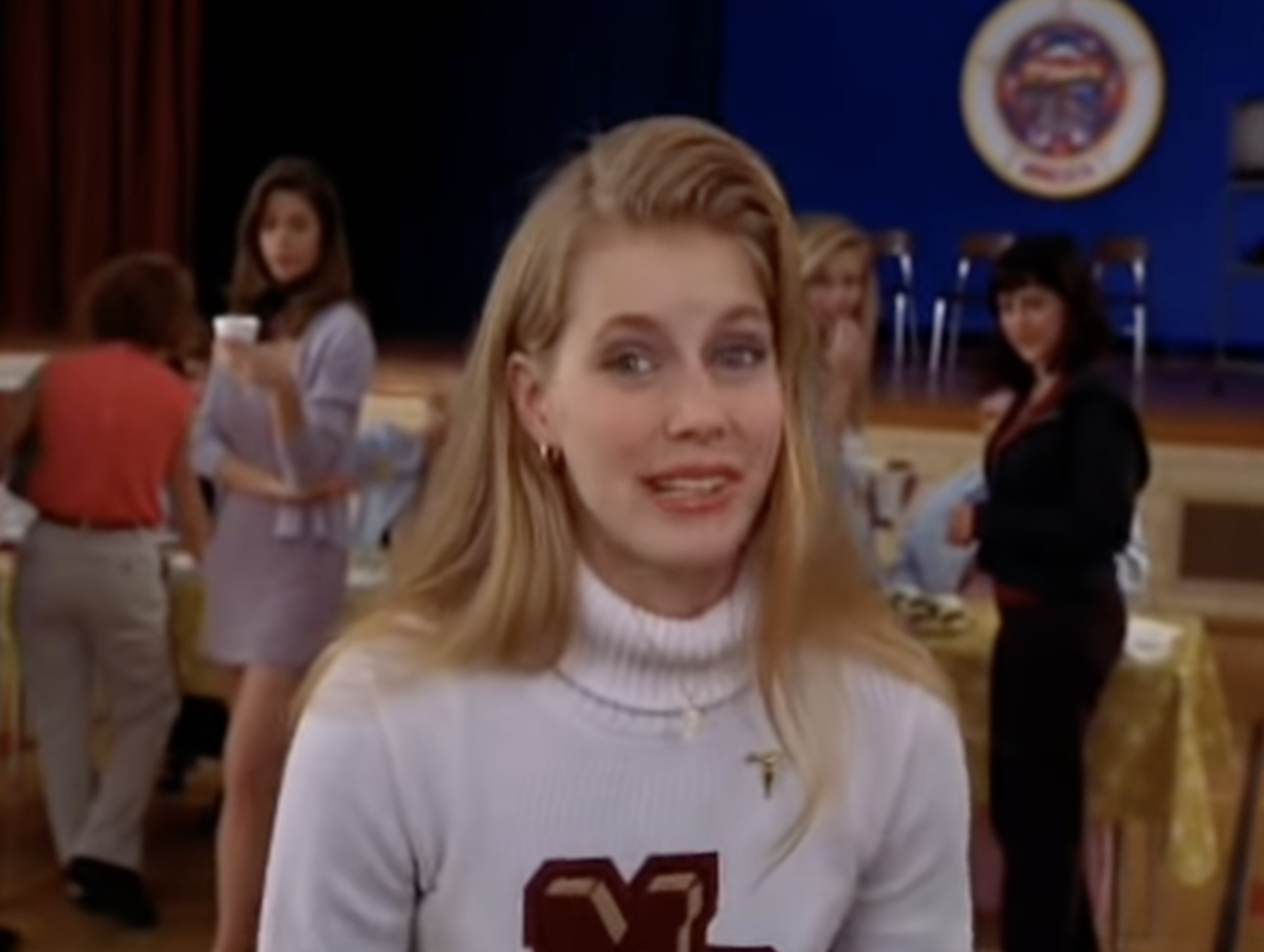 A young Amy Adams standing in a school hall and smiling at the camera