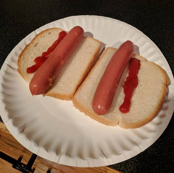 Two hot dogs on white bread with ketchup on it