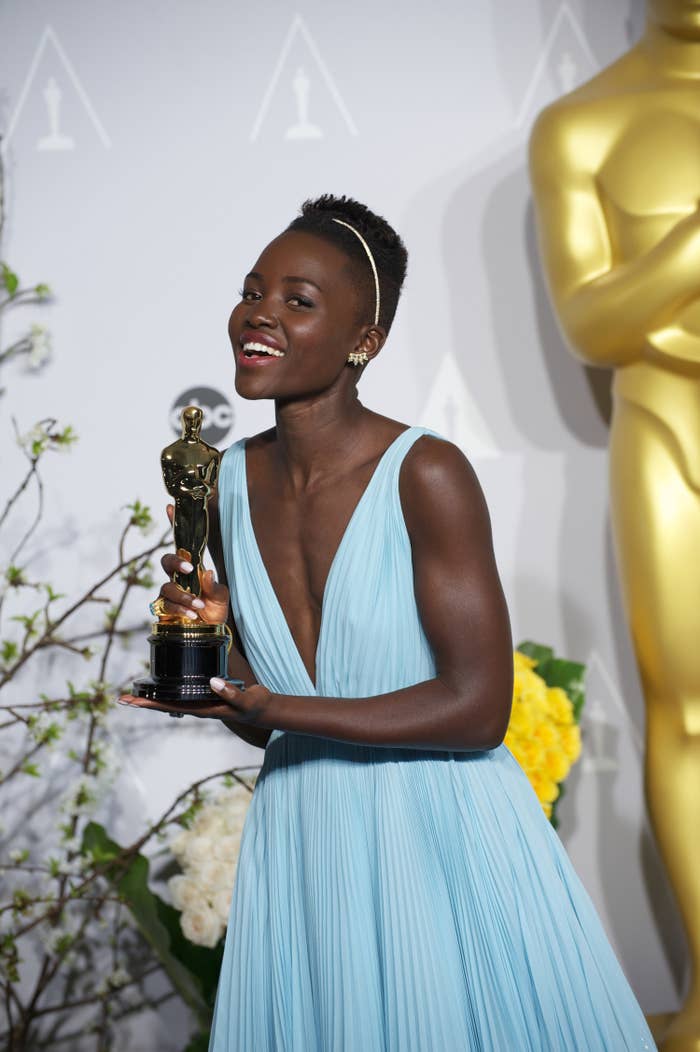 Lupita Nyong&#x27;o poses in a pale blue dress while smiling and holding an Oscar