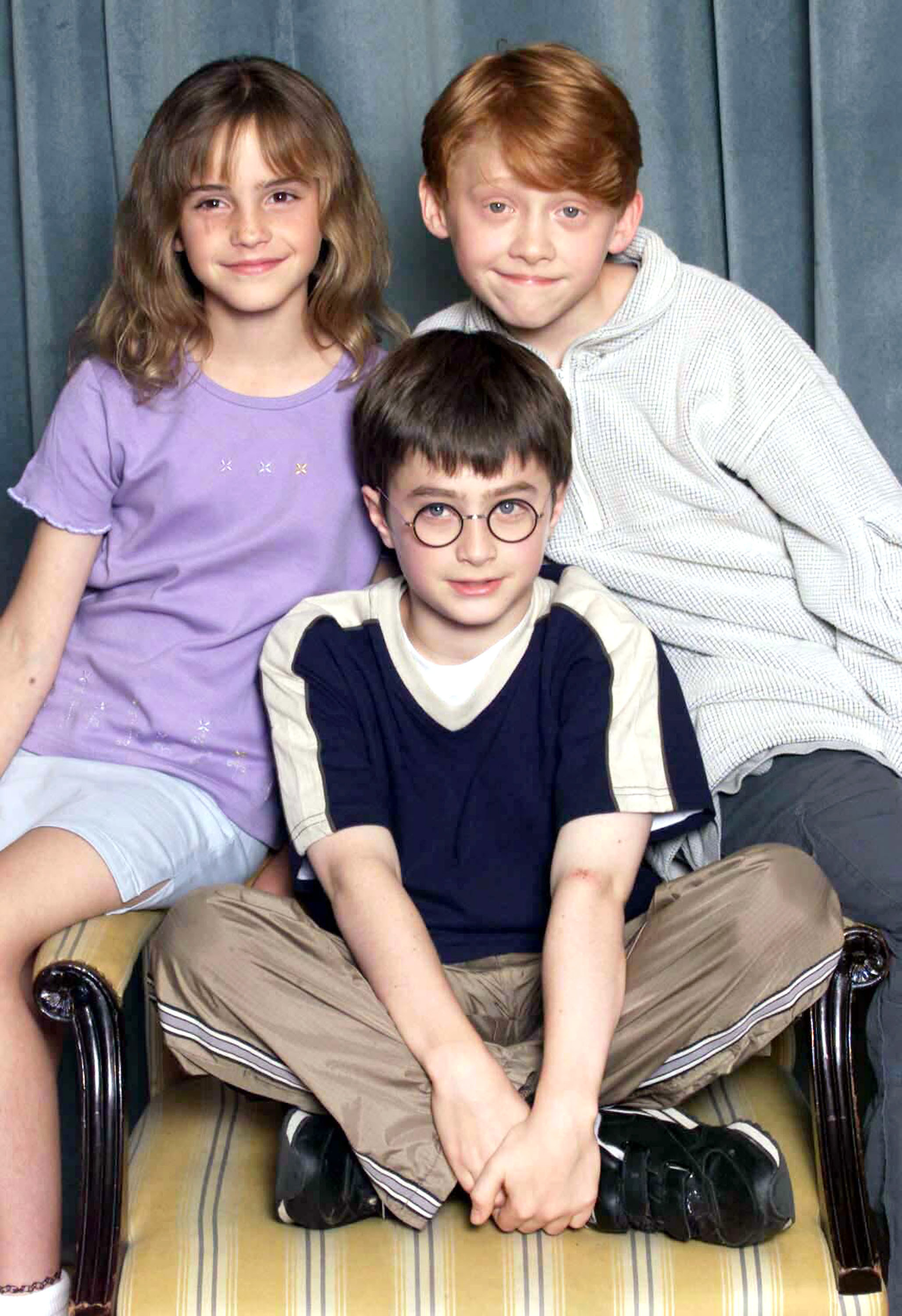 A pre-teen Daniel sitting on a chair as he&#x27;s flanked by Emma Watson on the left and Rupert Grint on the right