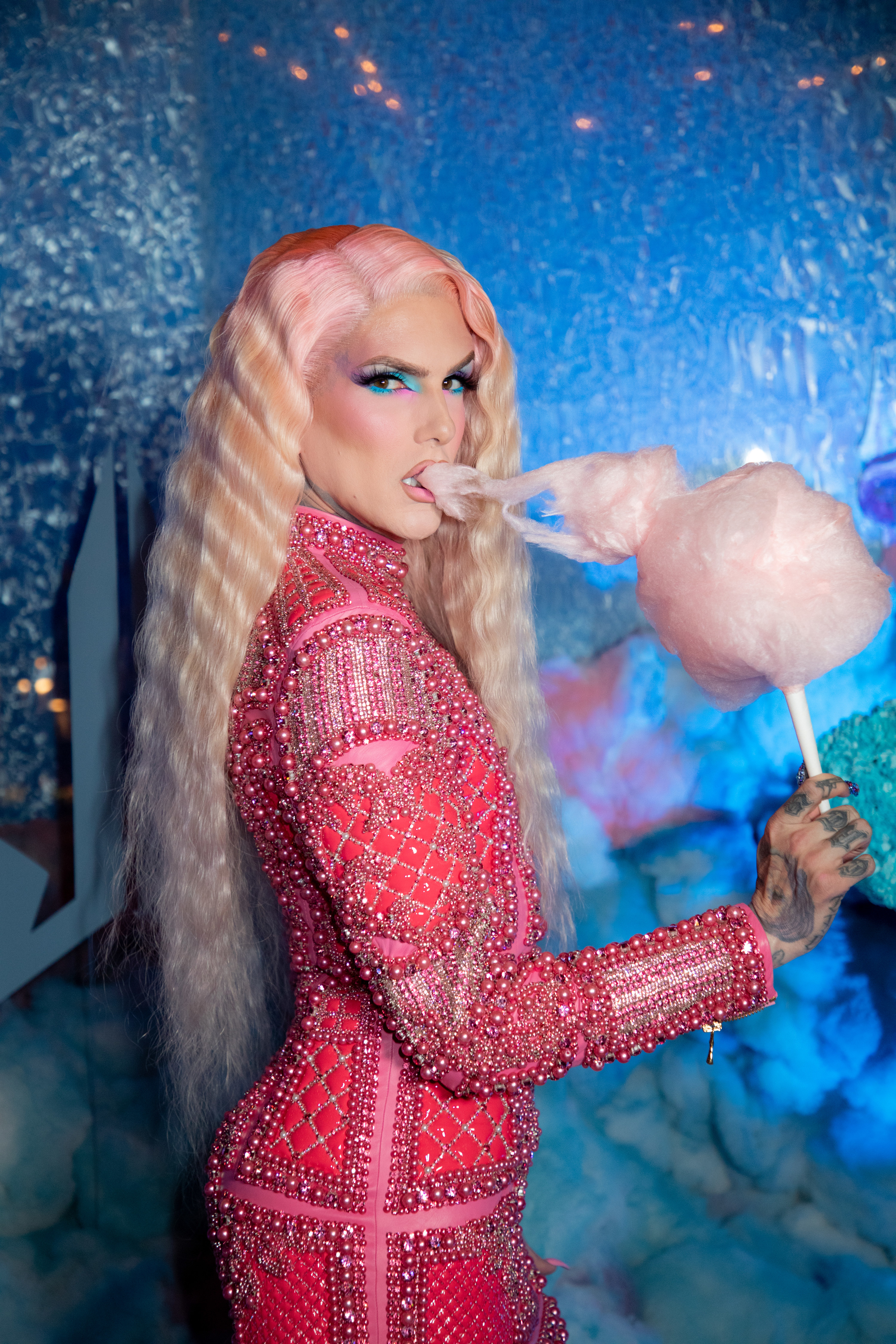 A photo of Jeffree Starr posing in a pink jewelled dress, long blonde hair, eating cotton candy