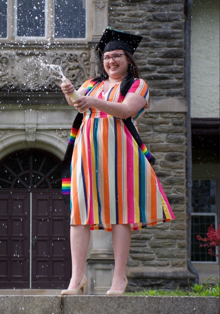 Reviewer spraying champagne in rainbow dress for graduation photoshoot